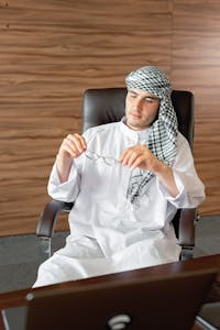 Middle Eastern man in traditional attire holding eyeglasses in a modern office.